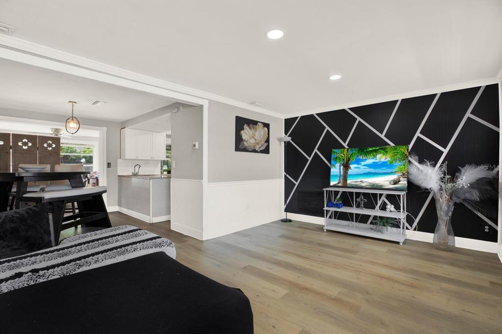 A living room features light wood flooring, white wainscoting, and a black geometric accent wall — 3920 BEACON SQUARE DRIVE, HOLIDAY, FL