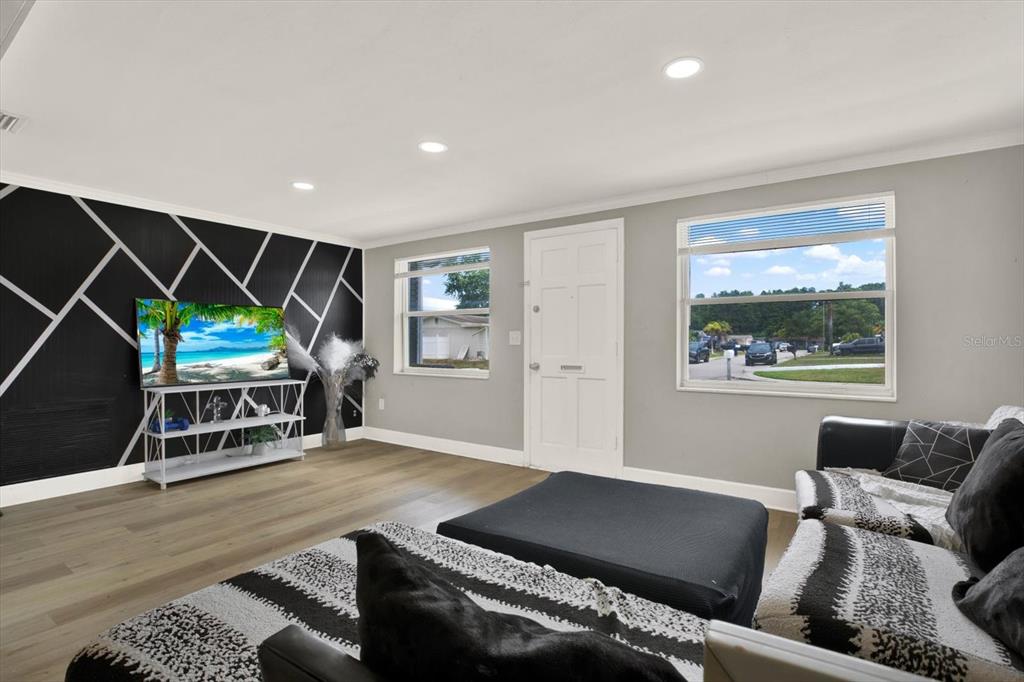 A living room features a black accent wall with geometric white lines and wood flooring — 3920 BEACON SQUARE DRIVE, HOLIDAY, FL