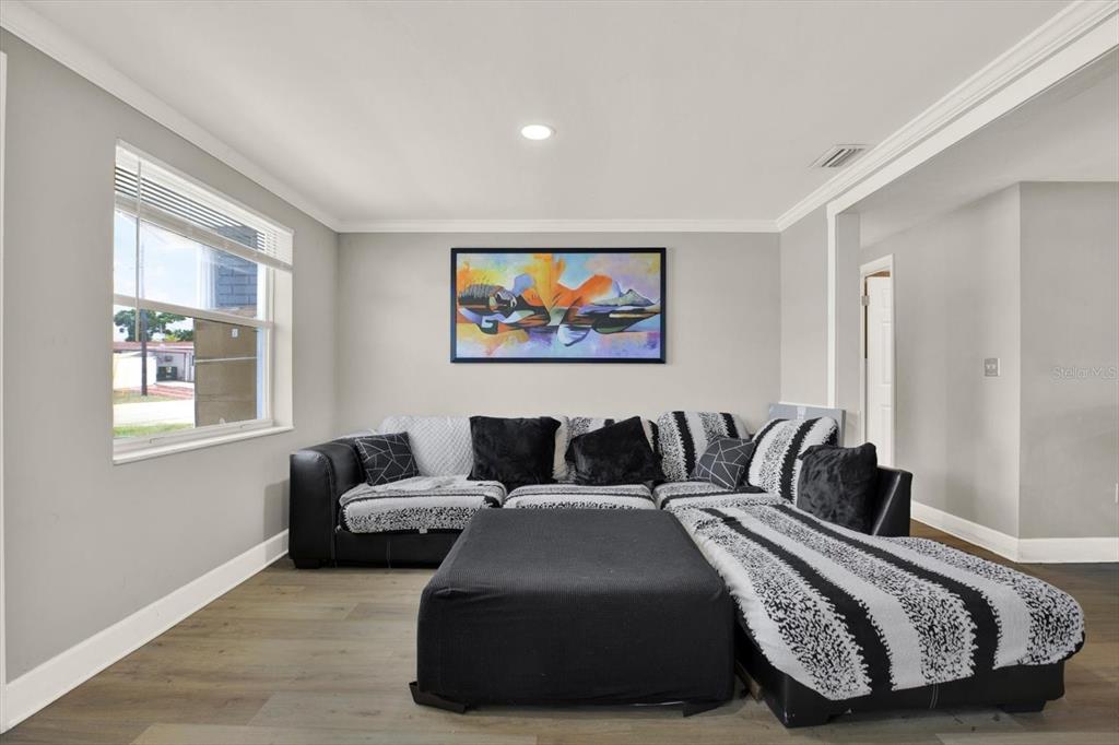 A living room features light gray walls, wood-look flooring, a large sectional sofa, and artwork — 3920 BEACON SQUARE DRIVE, HOLIDAY, FL