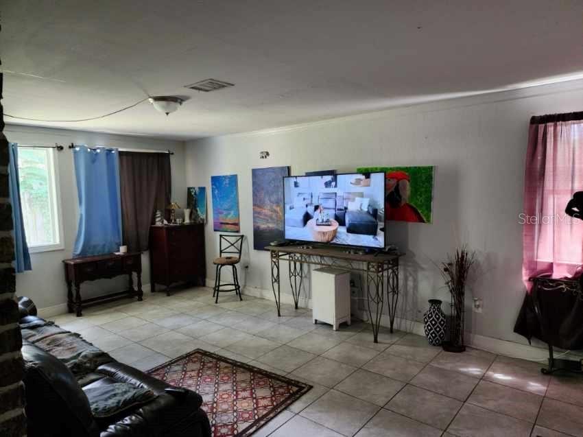 A living room with tile flooring, a television on a metal console, and wall art — 1149 HOLDEN AVENUE, ORLANDO, FL