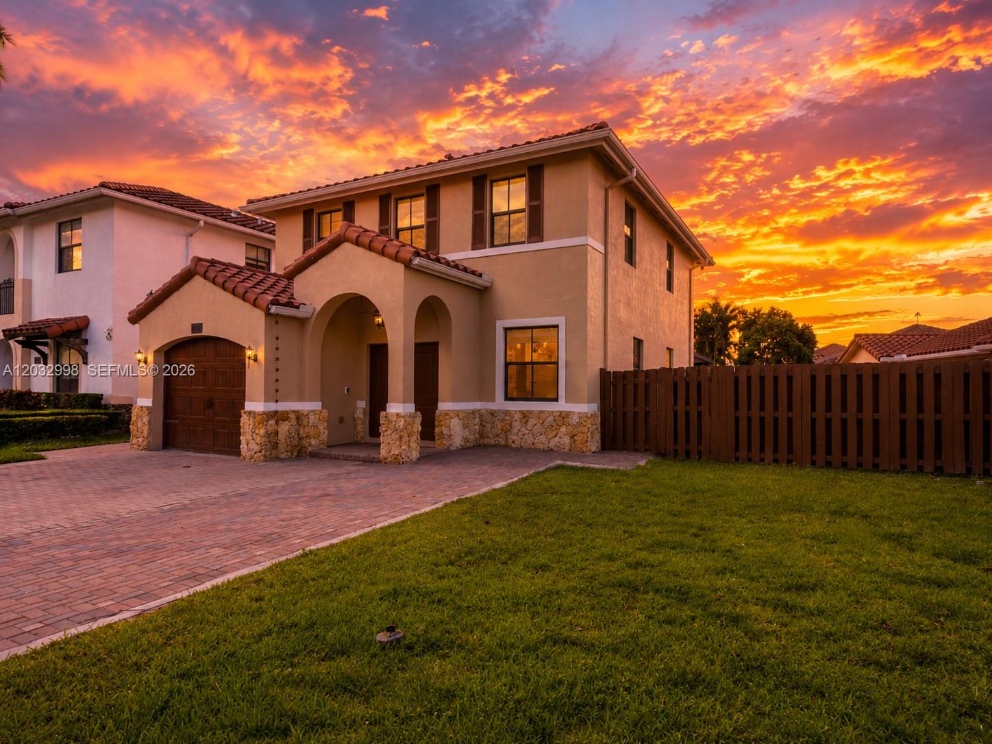A two-story stucco house with a stone base, tile roof, and attached garage at sunset — 9925 NW 10th St, Miami FL 33172, MIAMI, FL