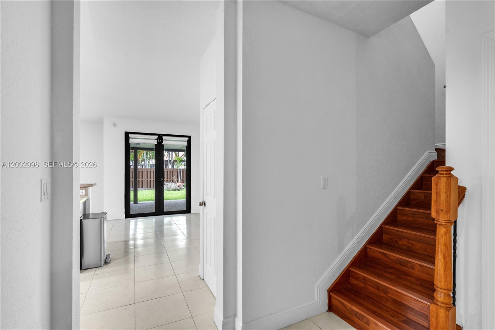 A view from a hallway toward a tiled room with glass doors and wooden stairs — 9925 NW 10th St, Miami FL 33172, MIAMI, FL