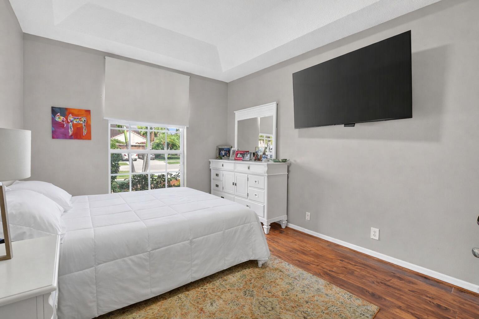 A bedroom features a white bed, a white dresser with a mirror, and a wall-mounted television — 18743 Cape Sable Drive, Boca Raton FL 33498, BOCA RATON, FL