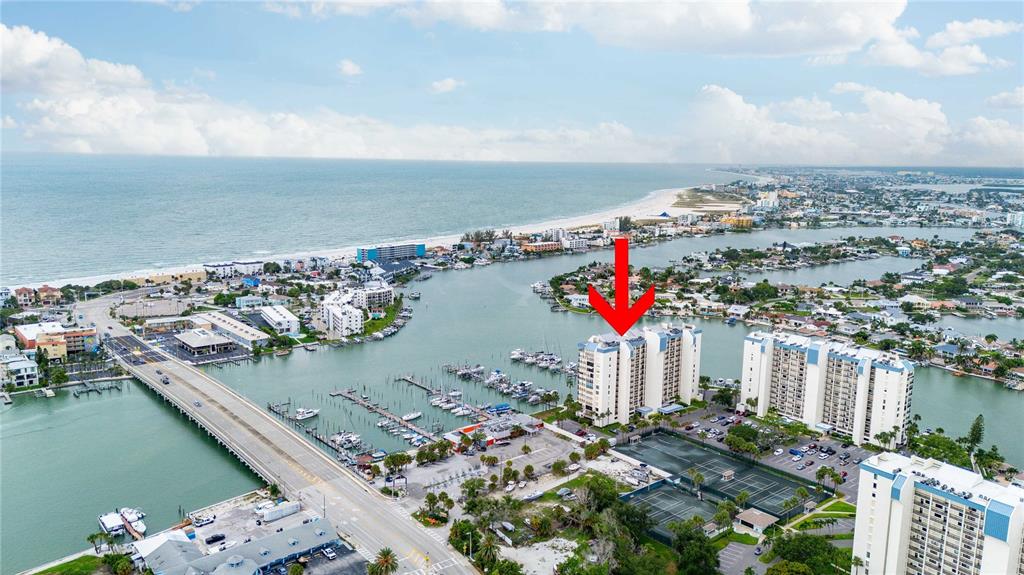 An aerial view shows a waterfront high-rise condominium building with a marina and tennis courts — 9525 BLIND PASS ROAD UNIT 206, ST PETERSBURG, FL