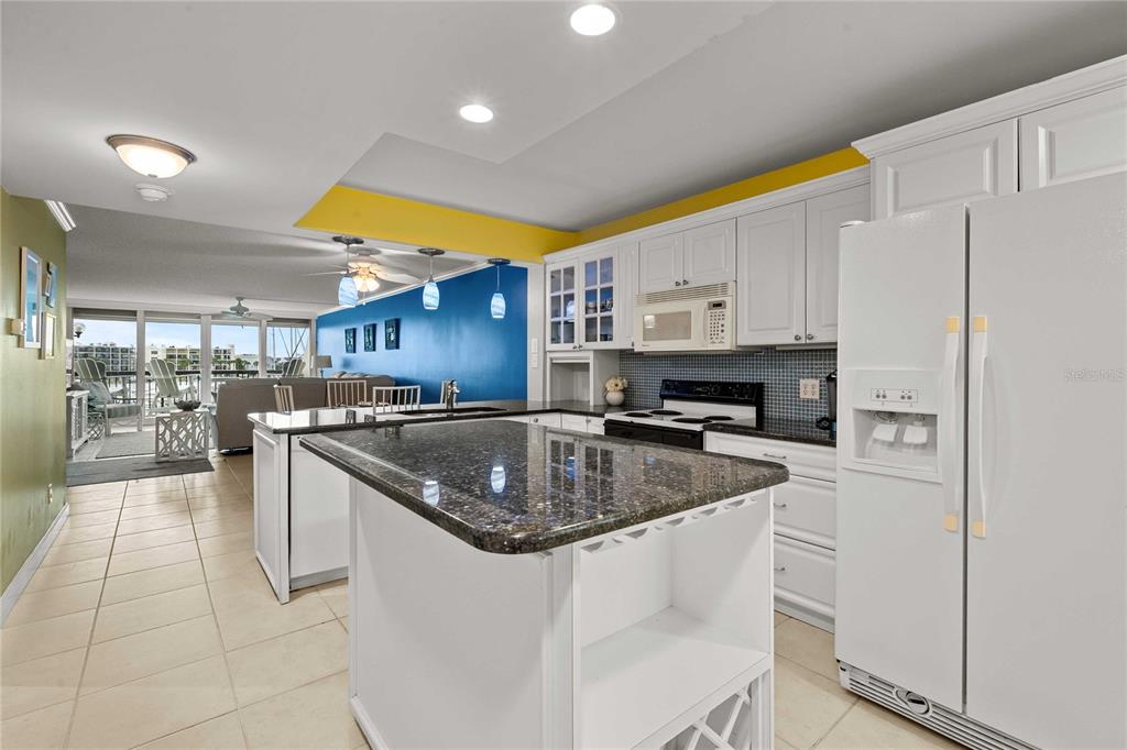 A kitchen with white cabinets, dark granite countertops, and a central island overlooks a living area — 9525 BLIND PASS ROAD UNIT 206, ST PETERSBURG, FL