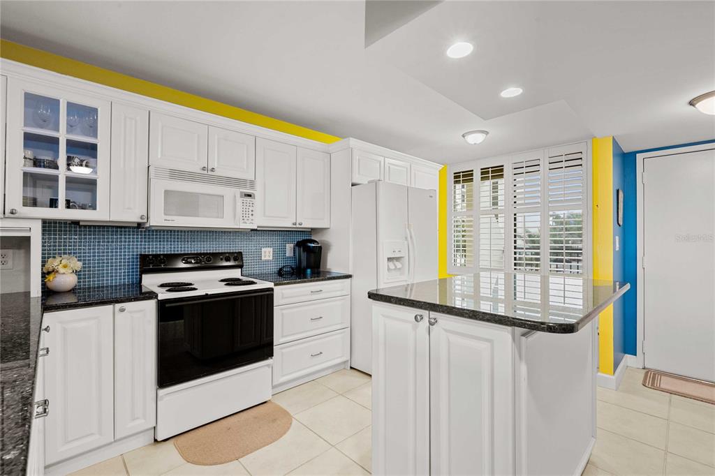 A kitchen features white cabinetry, a black stove, granite countertops, and blue tiled backsplashes — 9525 BLIND PASS ROAD UNIT 206, ST PETERSBURG, FL