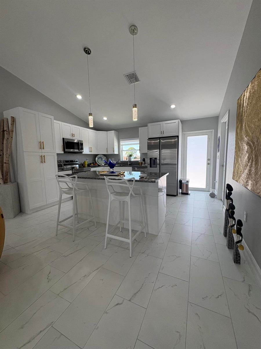A modern kitchen features white cabinets, a central island with bar stools, and marble-look flooring — 9019 S Castle Circle, FL 33935, FL