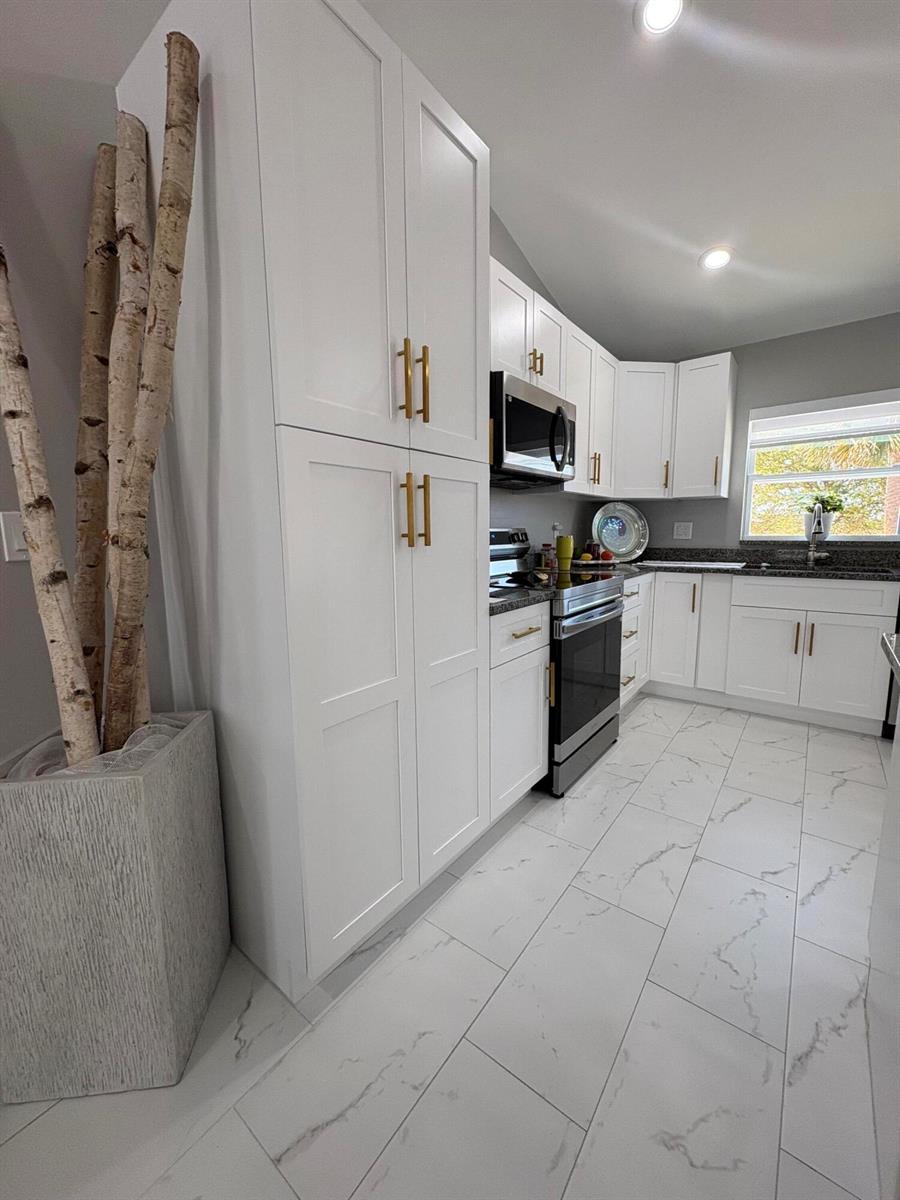 A kitchen features white shaker cabinets, gold hardware, marble-look tile flooring, and a decorative planter — 9019 S Castle Circle, FL 33935, FL