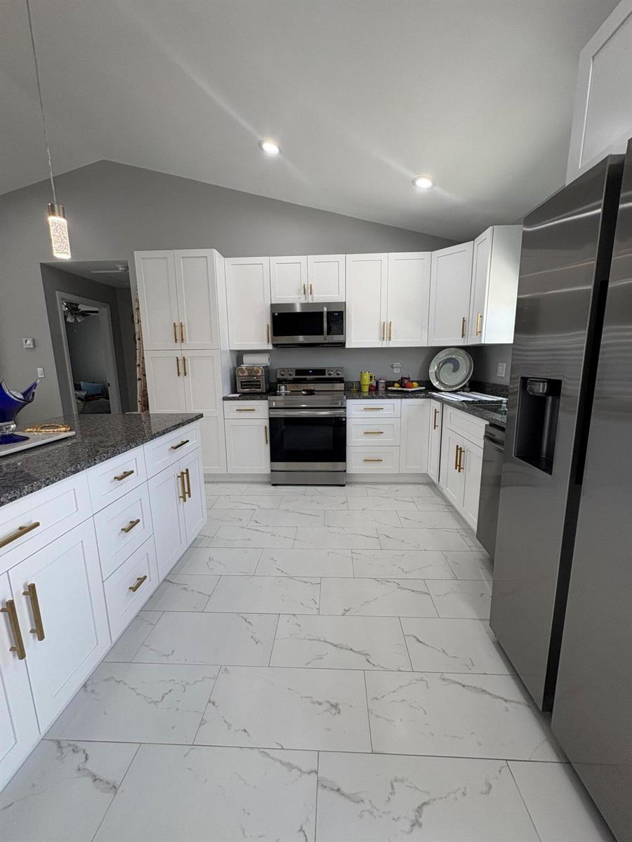 A modern kitchen features white cabinets, granite countertops, stainless steel appliances, and white marble-look flooring — 9019 S Castle Circle, FL 33935, FL