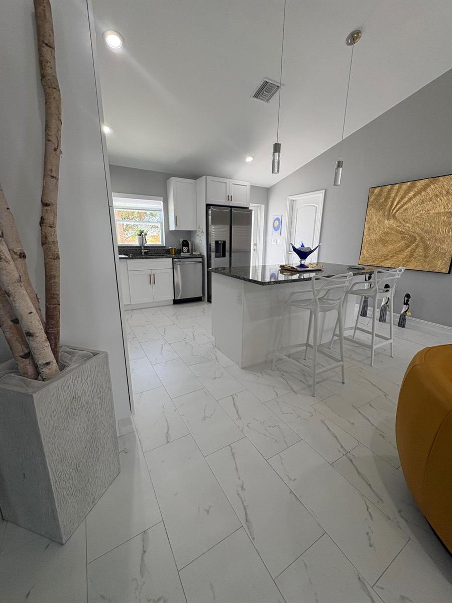 A kitchen features white cabinets, granite countertops, a center island, and white marble-look tile flooring — 9019 S Castle Circle, FL 33935, FL