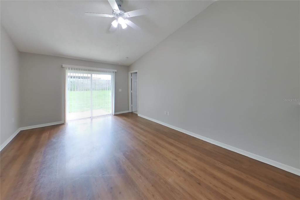 An empty room features light gray walls, wood-look flooring, a ceiling fan, and sliding doors — 7833 MANOR DRIVE, LAKELAND, FL