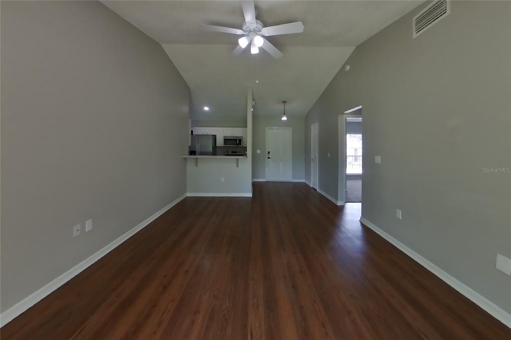 An open-concept living area features wood-look flooring, a ceiling fan, and a kitchen pass-through — 7833 MANOR DRIVE, LAKELAND, FL