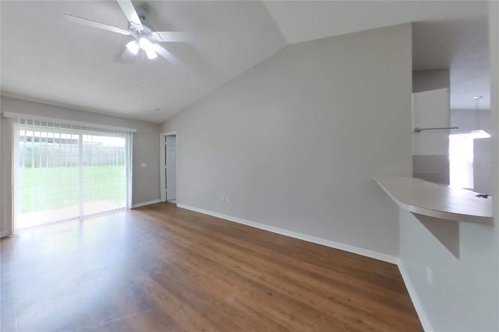 An empty living room features wood-look flooring, a vaulted ceiling, and a sliding glass door — 7833 MANOR DRIVE, LAKELAND, FL
