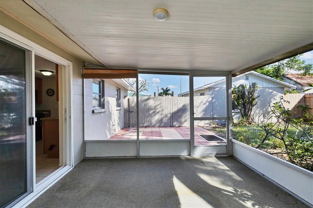 A covered screened-in porch with gray carpeting looks out onto a paved patio and yard — 25 1ST AVENUE, ENGLEWOOD, FL