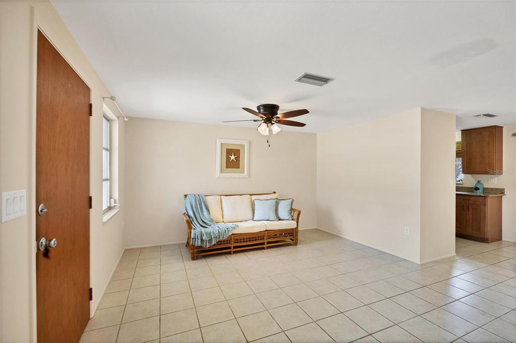A living room with tiled floors, a rattan sofa, and an adjacent kitchen area — 25 1ST AVENUE, ENGLEWOOD, FL