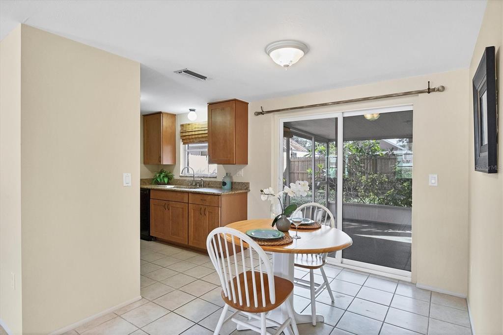 A dining area with a round wooden table sits adjacent to a kitchen with wood cabinets — 25 1ST AVENUE, ENGLEWOOD, FL