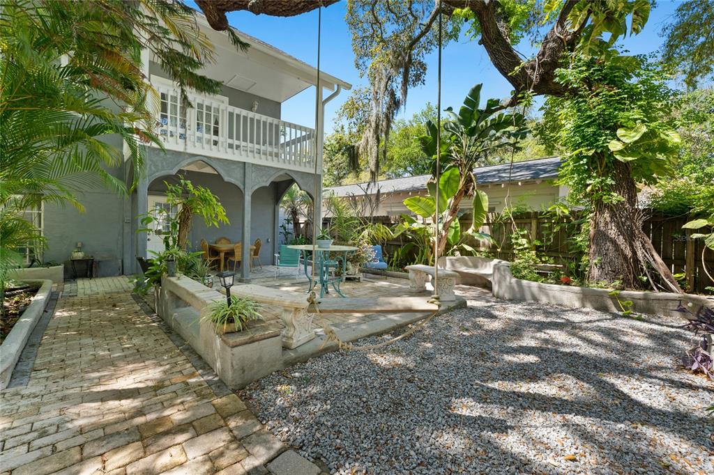 A backyard patio features a brick walkway, gravel area, stone benches, and a hanging swing — 515 CRYSTAL BEACH AVENUE, CRYSTAL BEACH, FL