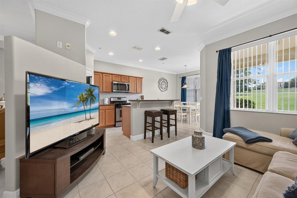 A living room with tile floors, a television, and an open kitchen with bar seating — 904 ASSEMBLY COURT, KISSIMMEE, FL