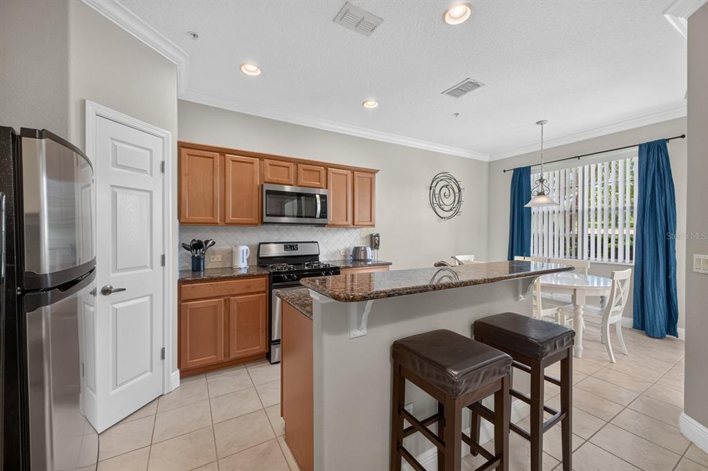 A kitchen with wood cabinets, stainless steel appliances, granite countertops, and a breakfast bar — 904 ASSEMBLY COURT, KISSIMMEE, FL