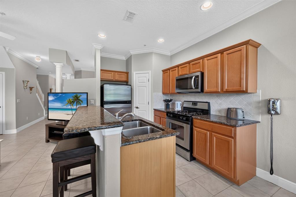 A kitchen features wood cabinets, granite countertops, a stainless steel stove, and a breakfast bar — 904 ASSEMBLY COURT, KISSIMMEE, FL