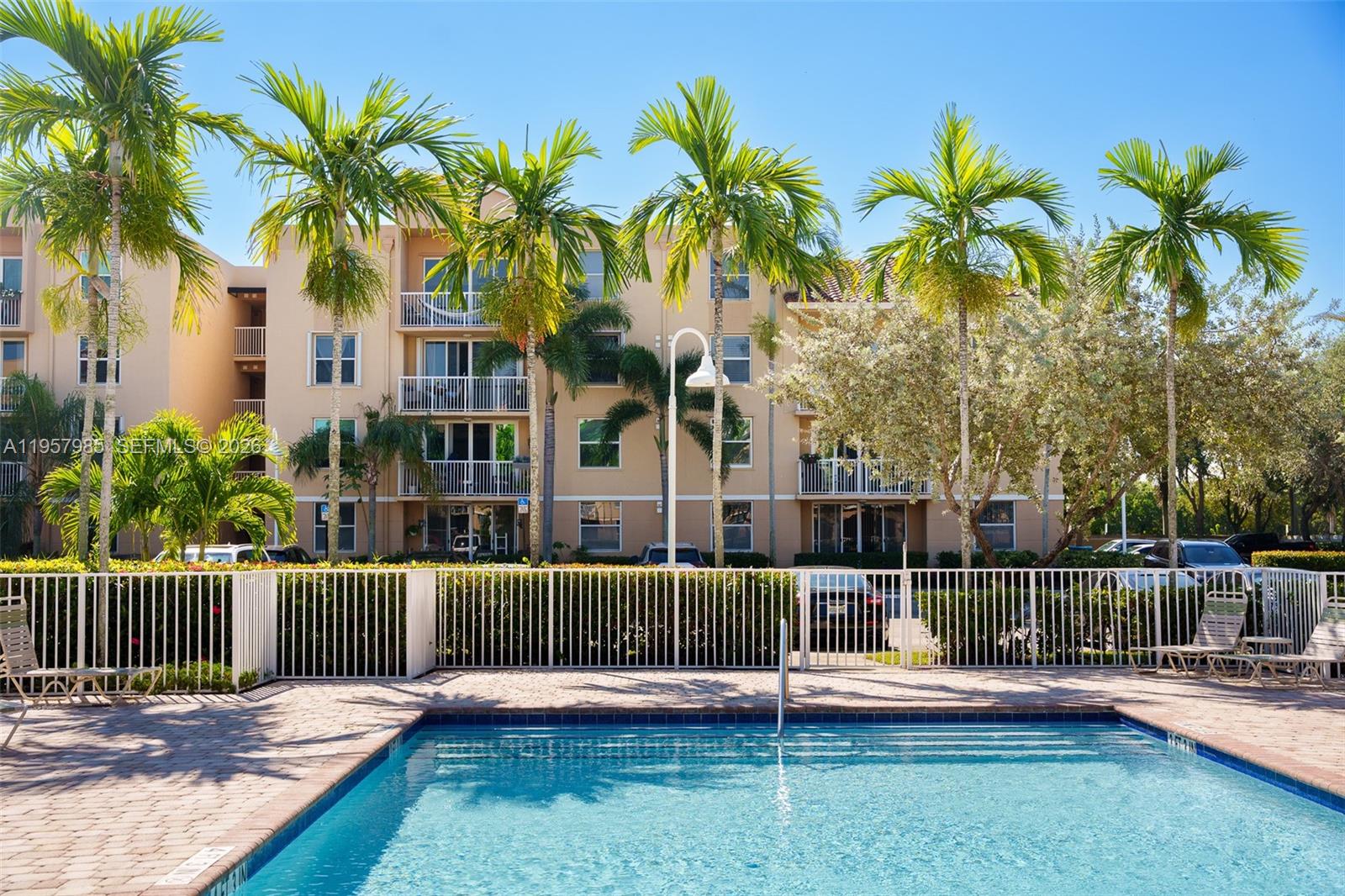 A swimming pool sits in the foreground before a multi-story apartment building with palm trees — 509 E Sheridan St # 3083, Dania Beach FL 33004, DANIA BEACH, FL