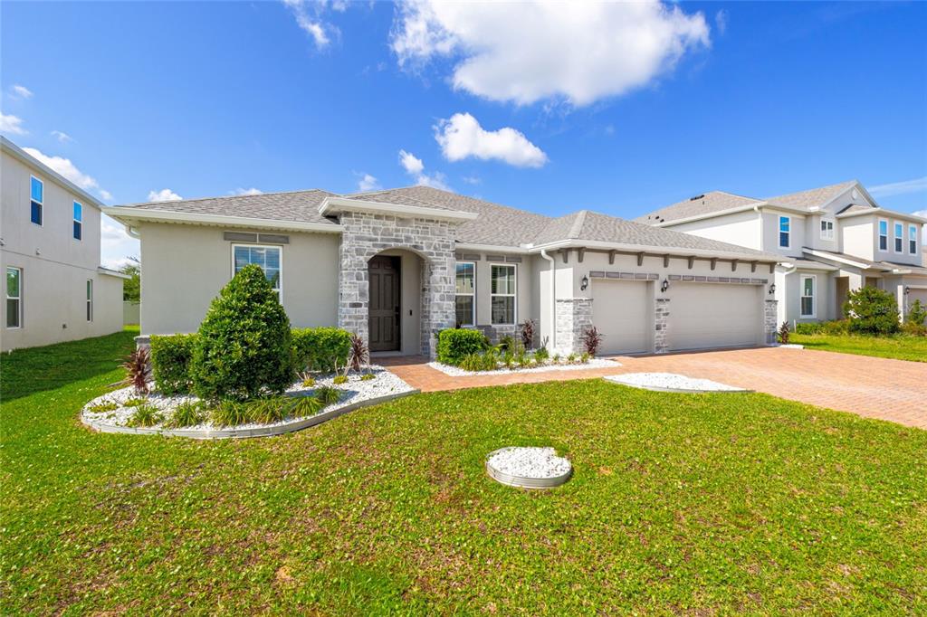 A single-story house with a stone facade, a three-car garage, and a landscaped front yard — 1325 BLARNEY STREET, CLERMONT, FL