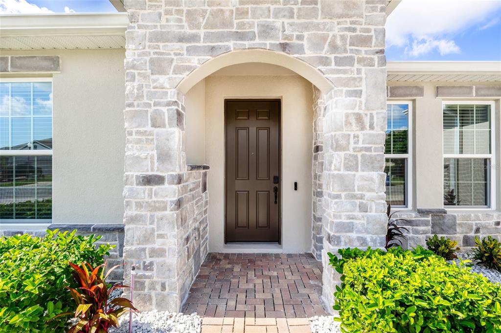 A brown front door is set within a stone-faced entryway with a brick porch — 1325 BLARNEY STREET, CLERMONT, FL