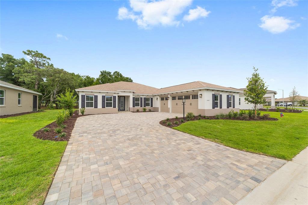 A single-story house with a paved driveway, tan exterior, and a three-car garage — 10787 SW 96TH LANE, OCALA, FL