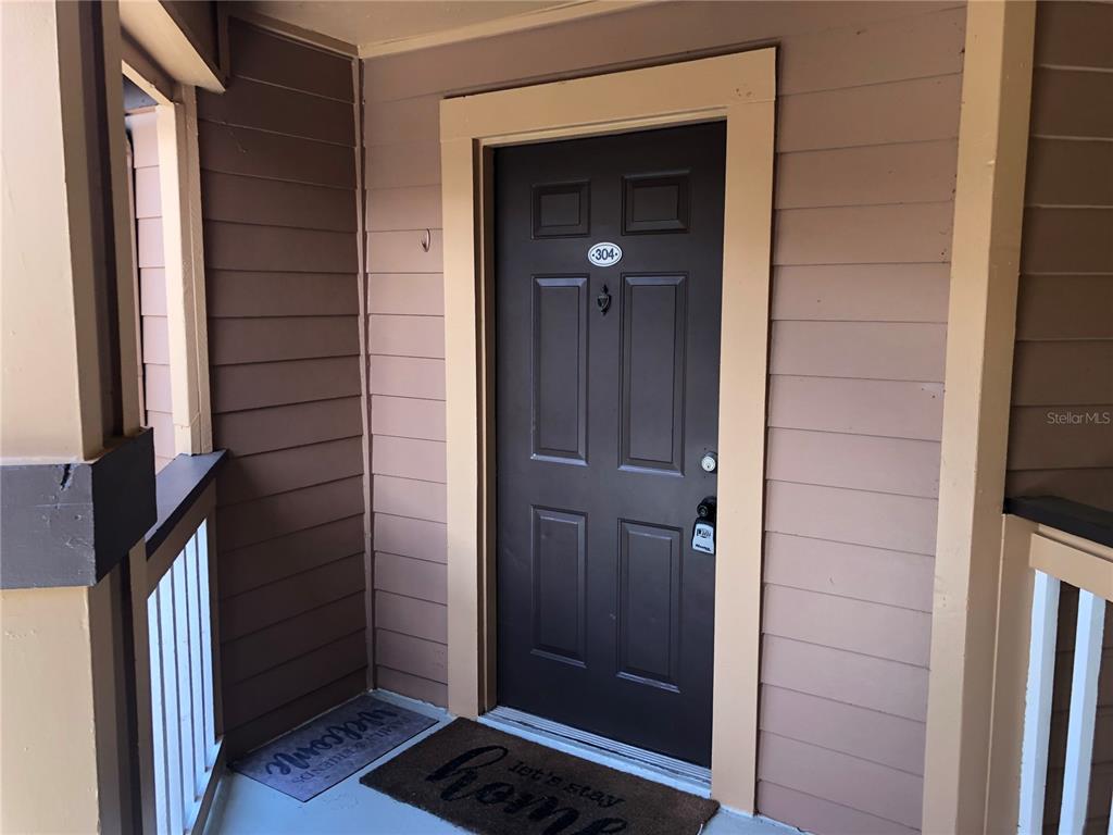 A dark brown front door with the number 304 is set in tan horizontal siding — 498 N PIN OAK PLACE UNIT 304, LONGWOOD, FL