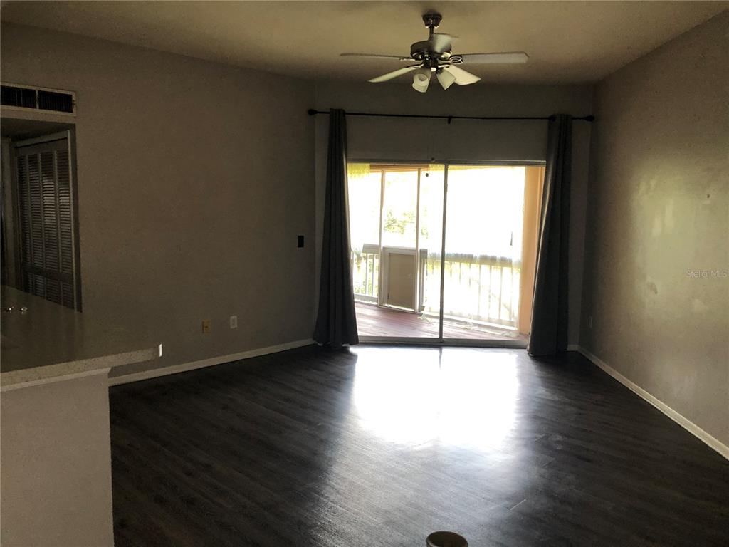 A living room with dark wood-look flooring, a ceiling fan, and a sliding glass door — 498 N PIN OAK PLACE UNIT 304, LONGWOOD, FL
