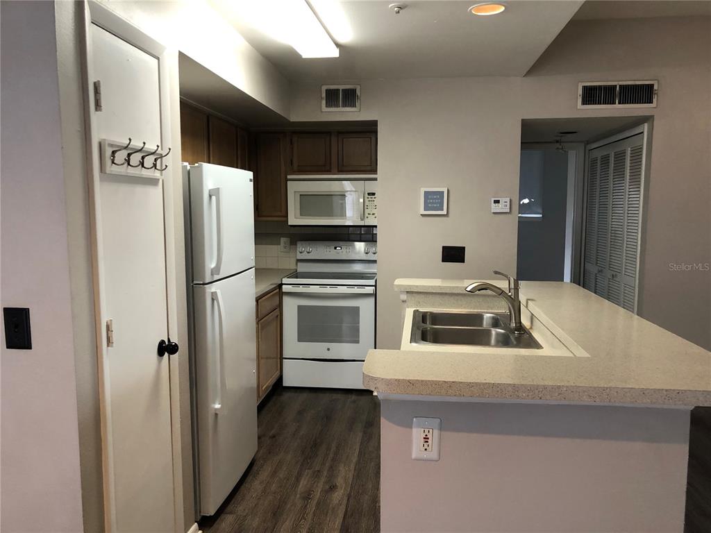 A kitchen features white appliances, wood cabinets, a breakfast bar, and wood-look flooring — 498 N PIN OAK PLACE UNIT 304, LONGWOOD, FL