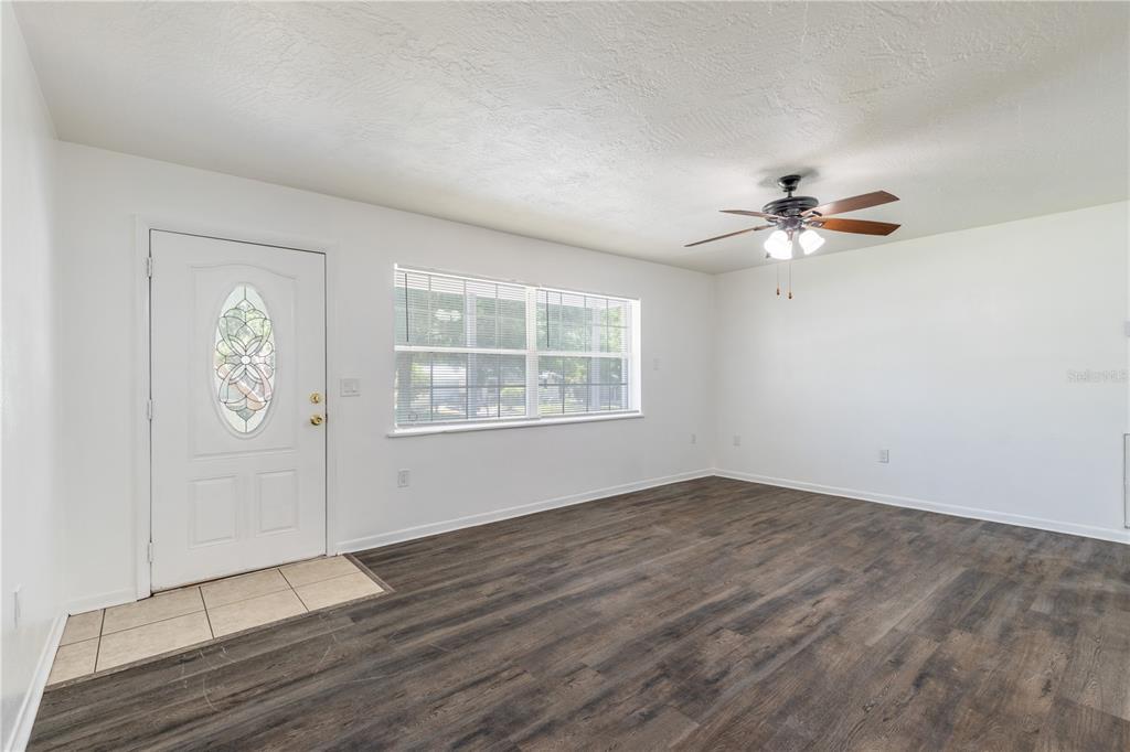 An empty living room features white walls, dark wood-look flooring, and a ceiling fan — 18 N HARRISON STREET, BEVERLY HILLS, FL