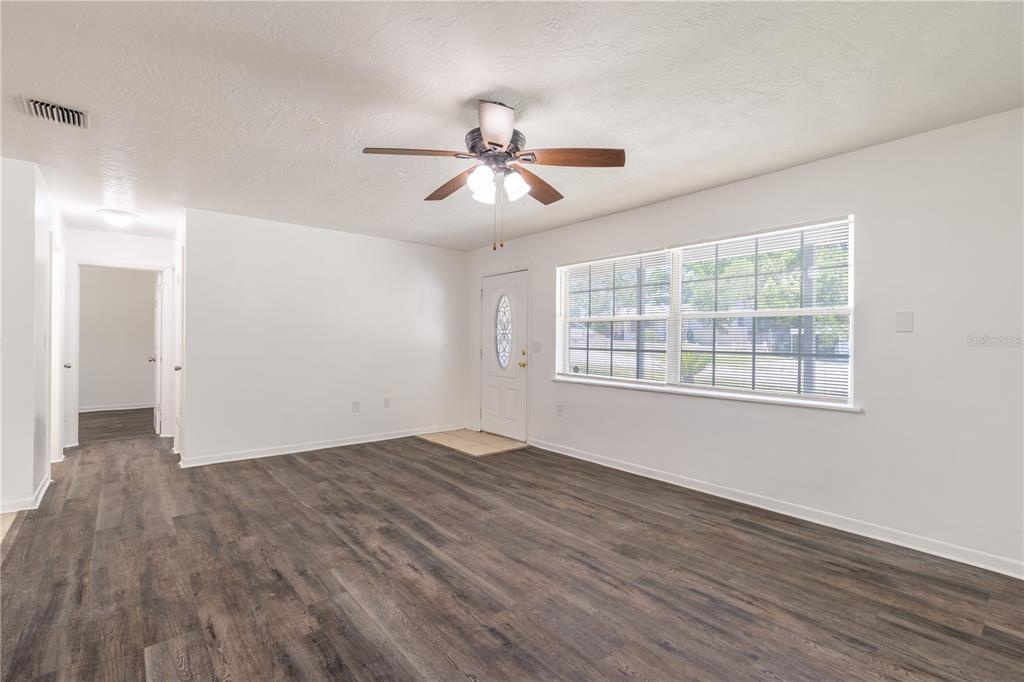 An empty living room features wood-look flooring, white walls, a ceiling fan, and a front door — 18 N HARRISON STREET, BEVERLY HILLS, FL