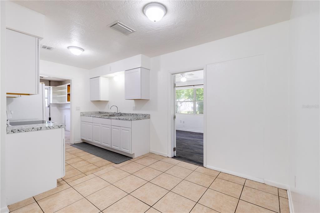 A kitchen with white cabinets, granite countertops, and beige tile flooring leads to another room — 18 N HARRISON STREET, BEVERLY HILLS, FL