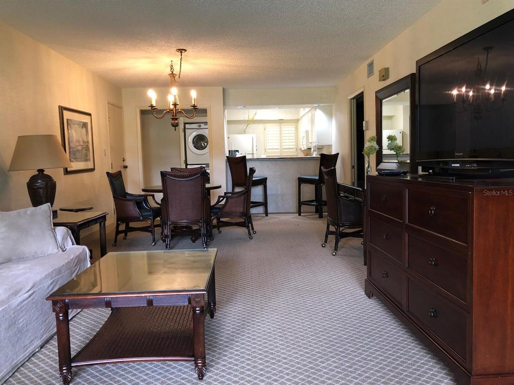 A living room and dining area with carpeted floors, a glass-topped coffee table, and bar seating — 29129 BAY HOLLOW DRIVE UNIT 3203, WESLEY CHAPEL, FL