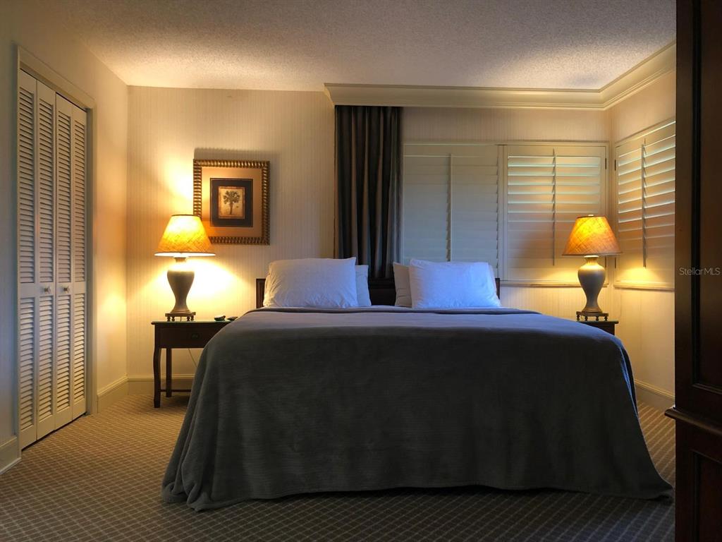 A bedroom features a bed with a gray cover, two lamps, and white louvered shutters — 29129 BAY HOLLOW DRIVE UNIT 3203, WESLEY CHAPEL, FL