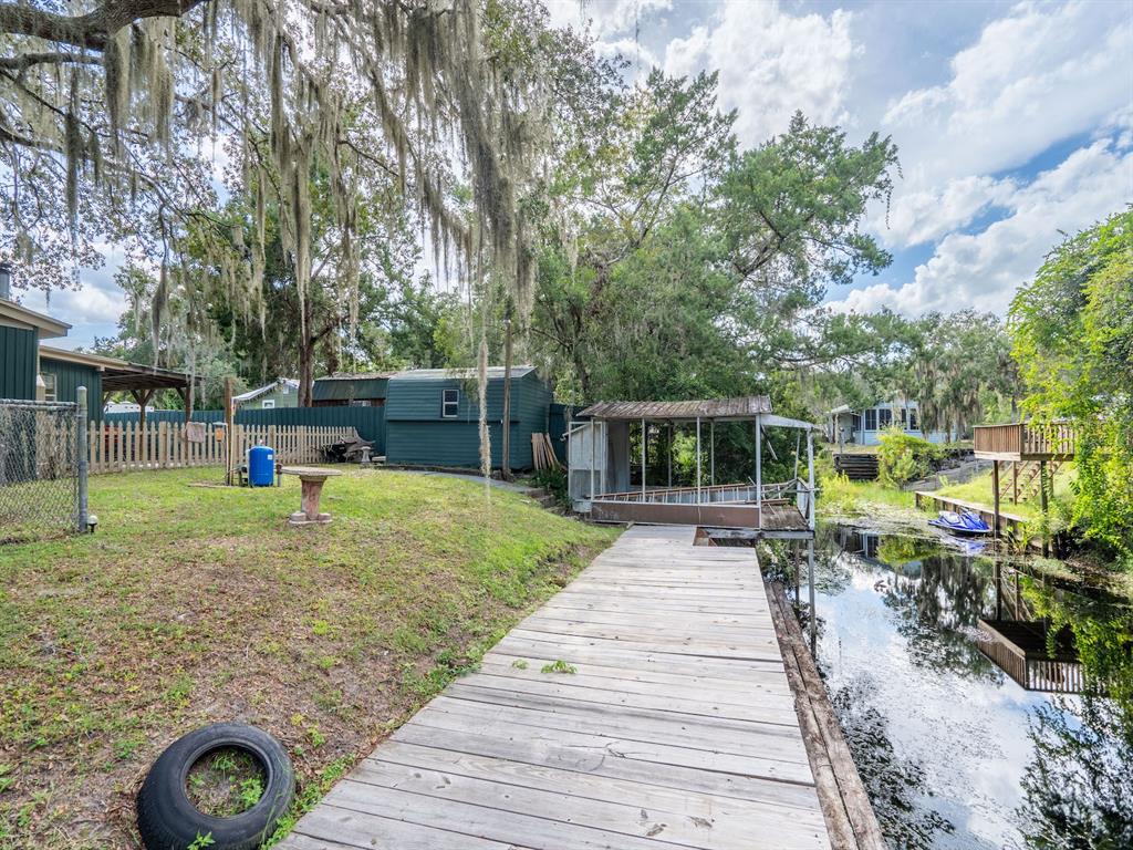 A wooden dock extends along a canal next to a grassy yard with a shed — 24855 NE 135 STREET, SALT SPRINGS, FL