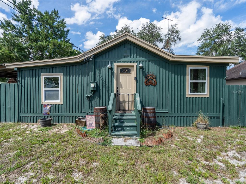 A green, single-story cabin with a tan door, wooden steps, and two barrel planters — 24855 NE 135 STREET, SALT SPRINGS, FL
