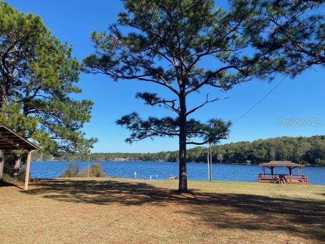 A grassy yard with pine trees overlooks a lake featuring a wooden gazebo — LOT 49 UNIT O&P, DEFUNIAK SPRINGS, FL