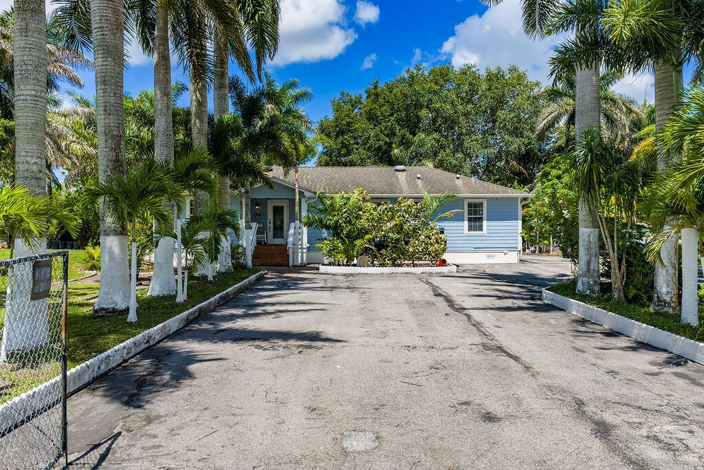 A light blue single-story house with a paved driveway surrounded by numerous tall palm trees — 6929 N 120th Ave Avenue N, FL 33412, FL