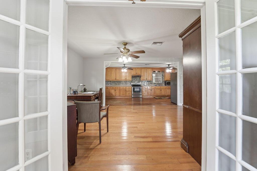 A view through French doors into a home office and an open-concept kitchen with wood flooring — 6929 N 120th Ave Avenue N, FL 33412, FL