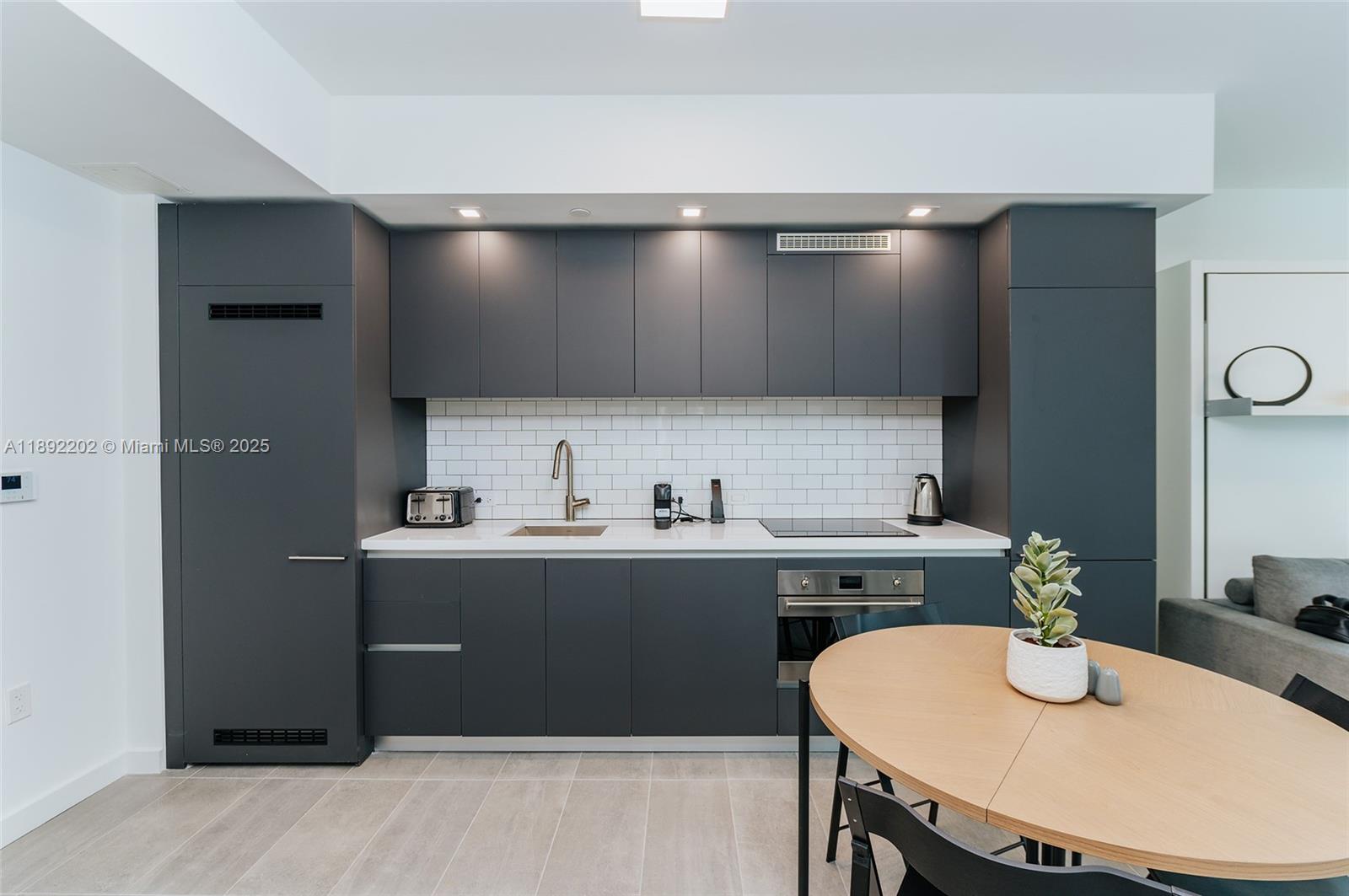A modern kitchen features dark gray cabinetry, white subway tile backsplash, and a round dining table — 227 NE 2nd St # 2508, Miami FL 33132, MIAMI, FL