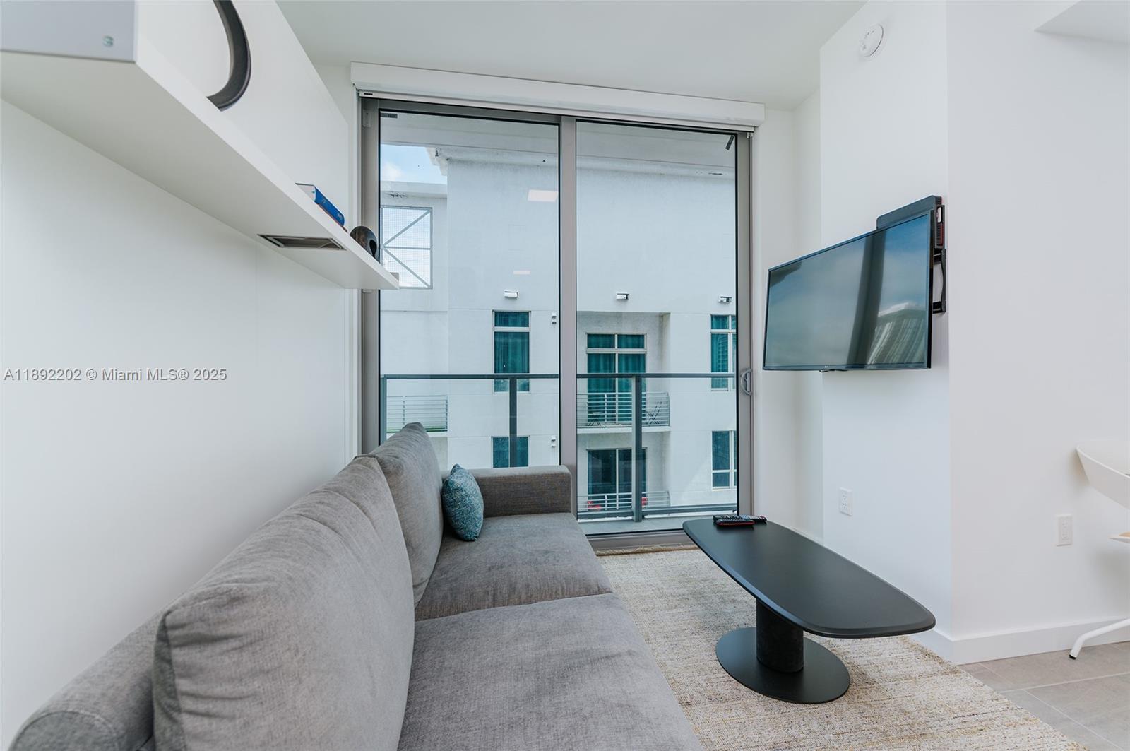 A living room features a gray sofa, a black coffee table, and a wall-mounted television — 227 NE 2nd St # 2508, Miami FL 33132, MIAMI, FL