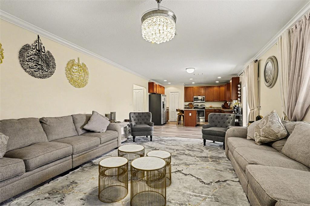 A living room with two gray sofas, two armchairs, and a kitchen in the background — 1688 ATTILBURGH BOULEVARD, WEST MELBOURNE, FL