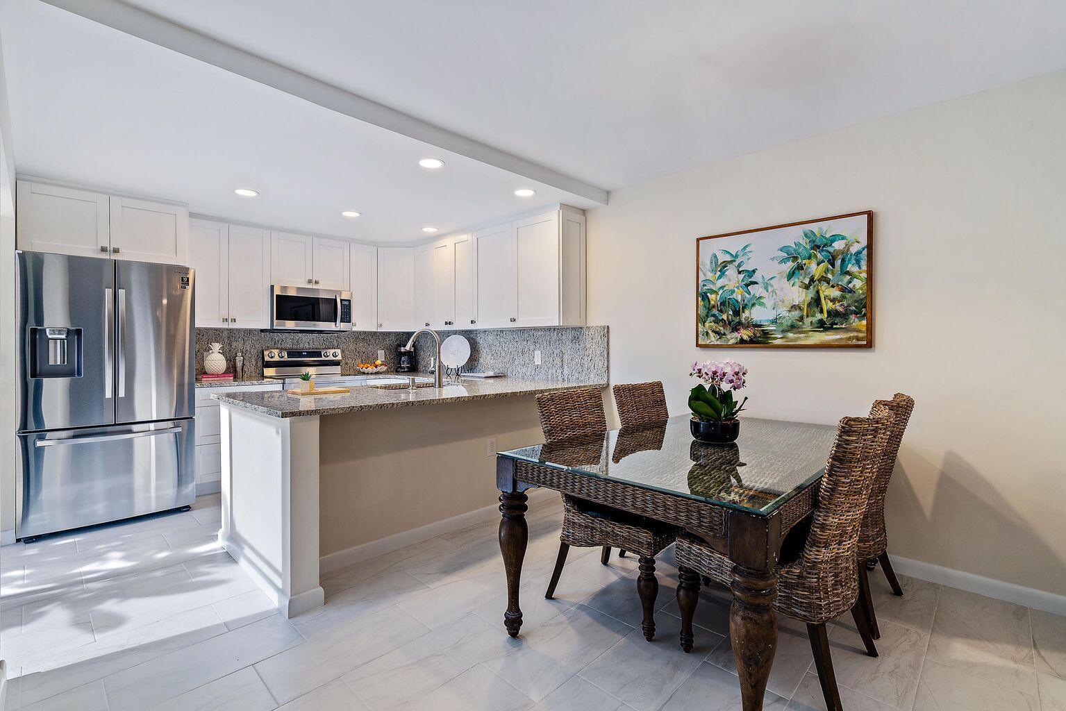 A kitchen with white cabinets and granite countertops sits adjacent to a glass-topped dining table — 2316 23rd Court, Jupiter FL 33477, JUPITER, FL