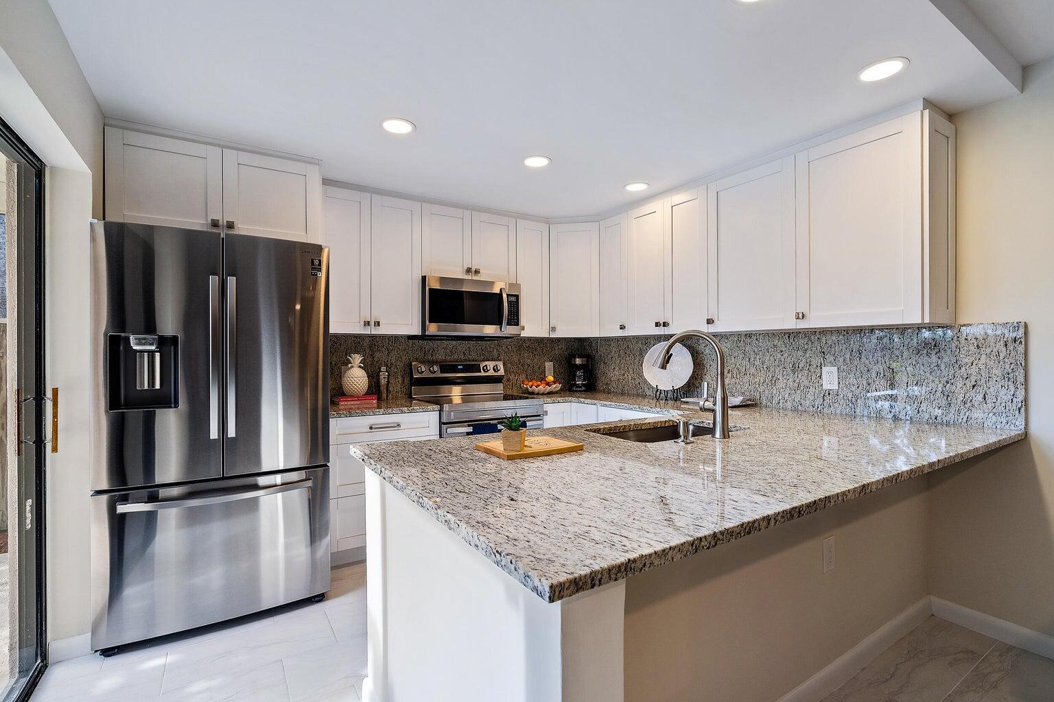 A kitchen features white cabinets, granite countertops, stainless steel appliances, and a peninsula with sink — 2316 23rd Court, Jupiter FL 33477, JUPITER, FL