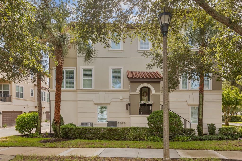 A three-story beige townhouse with a tiled entryway, multiple windows, and surrounding palm trees — 801 LOBELIA DRIVE, LAKE MARY, FL