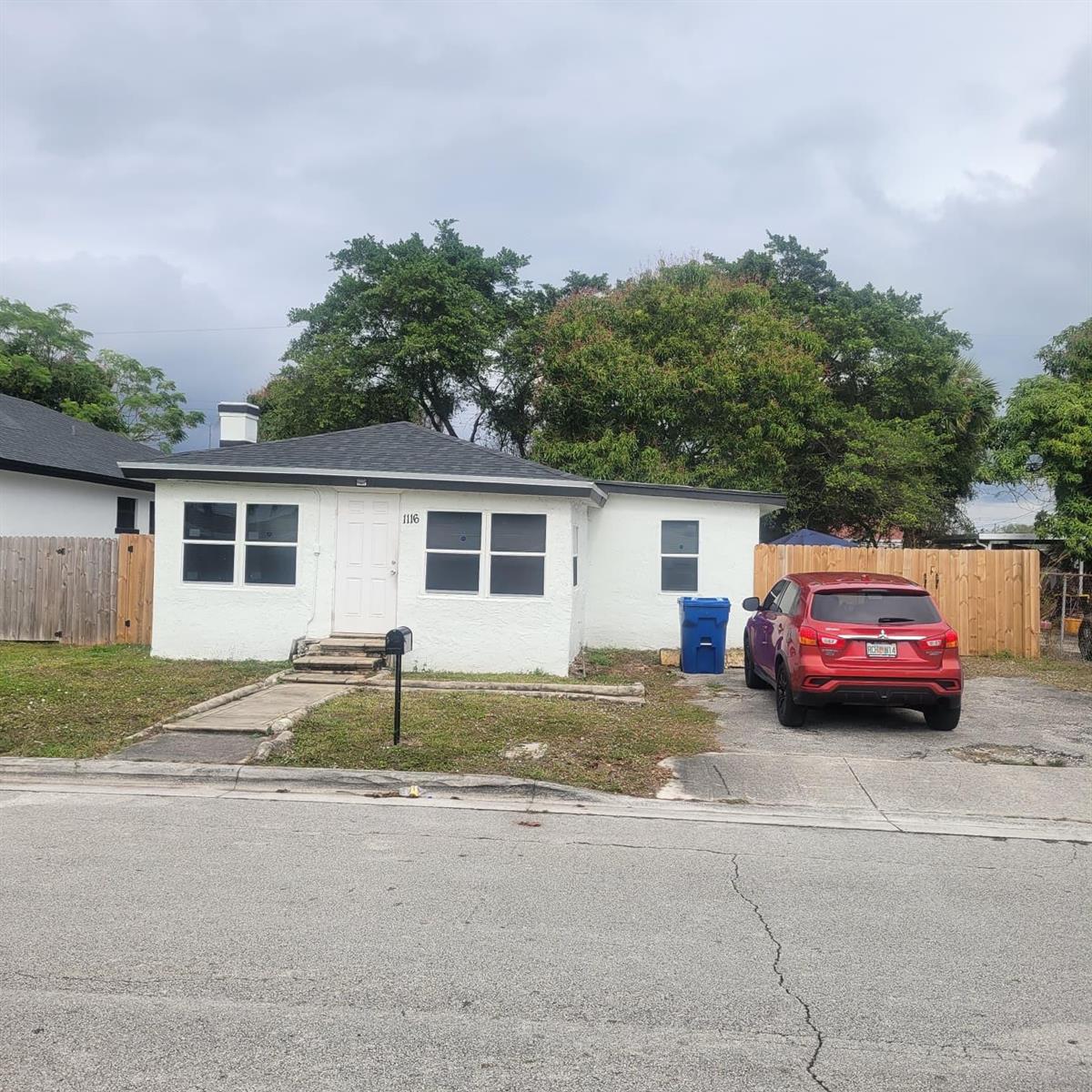A single-story white house with a dark roof, a red car, and a wooden fence — 1116 W 32nd Street, Riviera Beach FL 33404, RIVIERA BEACH, FL
