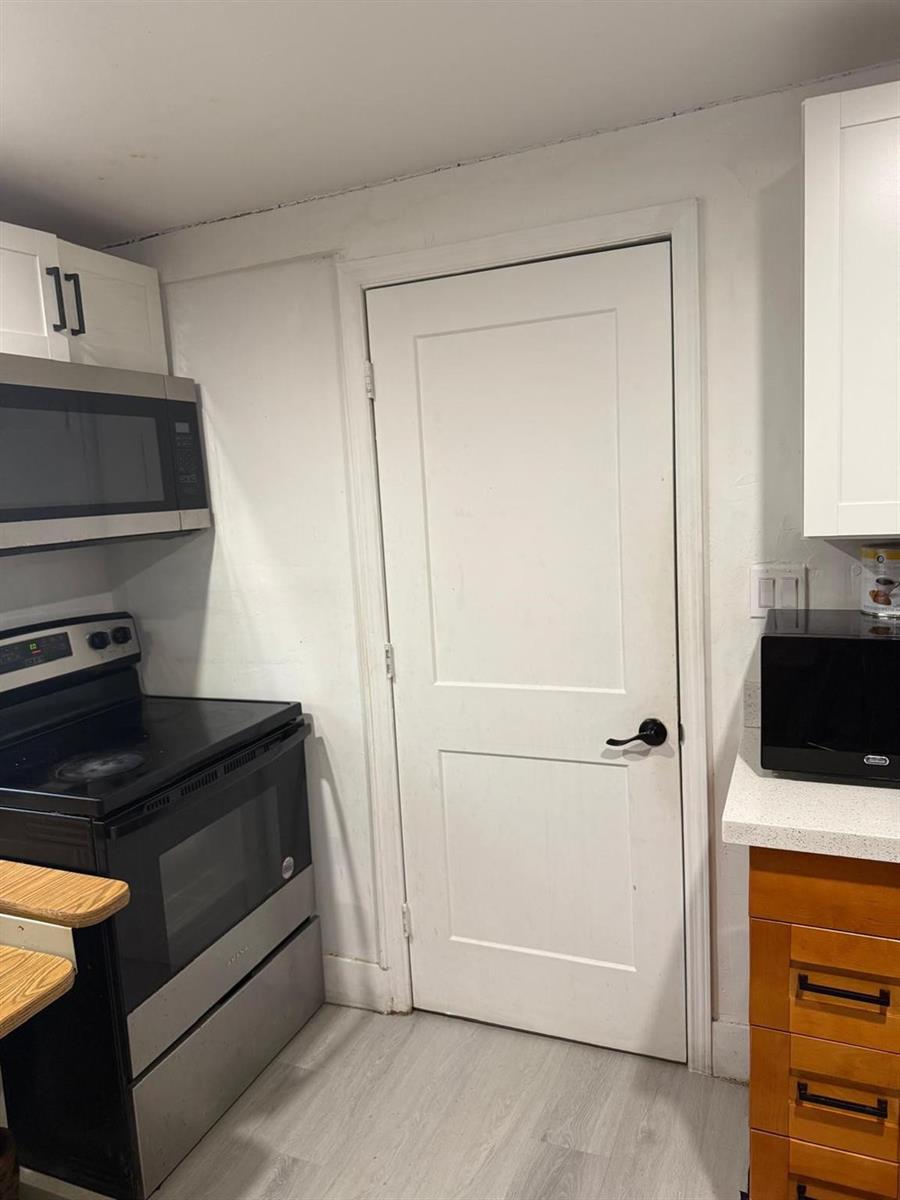 A kitchen features a stainless steel microwave, a black stove, white cabinets, and a white door — 1116 W 32nd Street, Riviera Beach FL 33404, RIVIERA BEACH, FL
