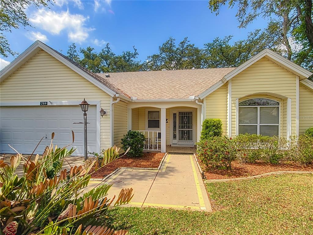 A single-story yellow house with a two-car garage and a paved walkway to the entrance — 208 DESOTA COURT, LADY LAKE, FL